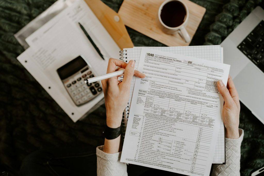 Person reviewing financial documents with a calculator and laptop on a desk