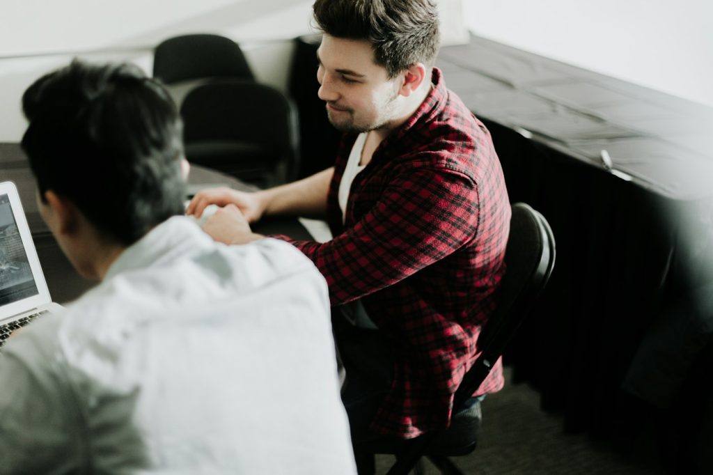 Two men shaking hands across a desk in a small office
