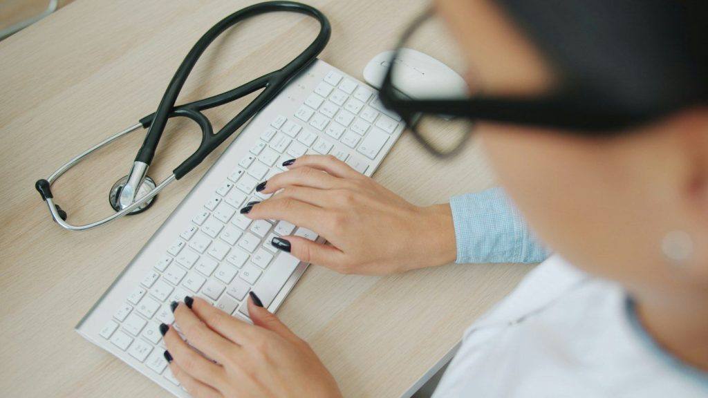 Doctor typing at a desk computer with a stethoscope beside the keyboard