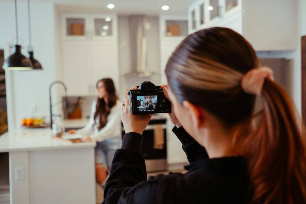Woman photographing herself with a phone in a home kitchen