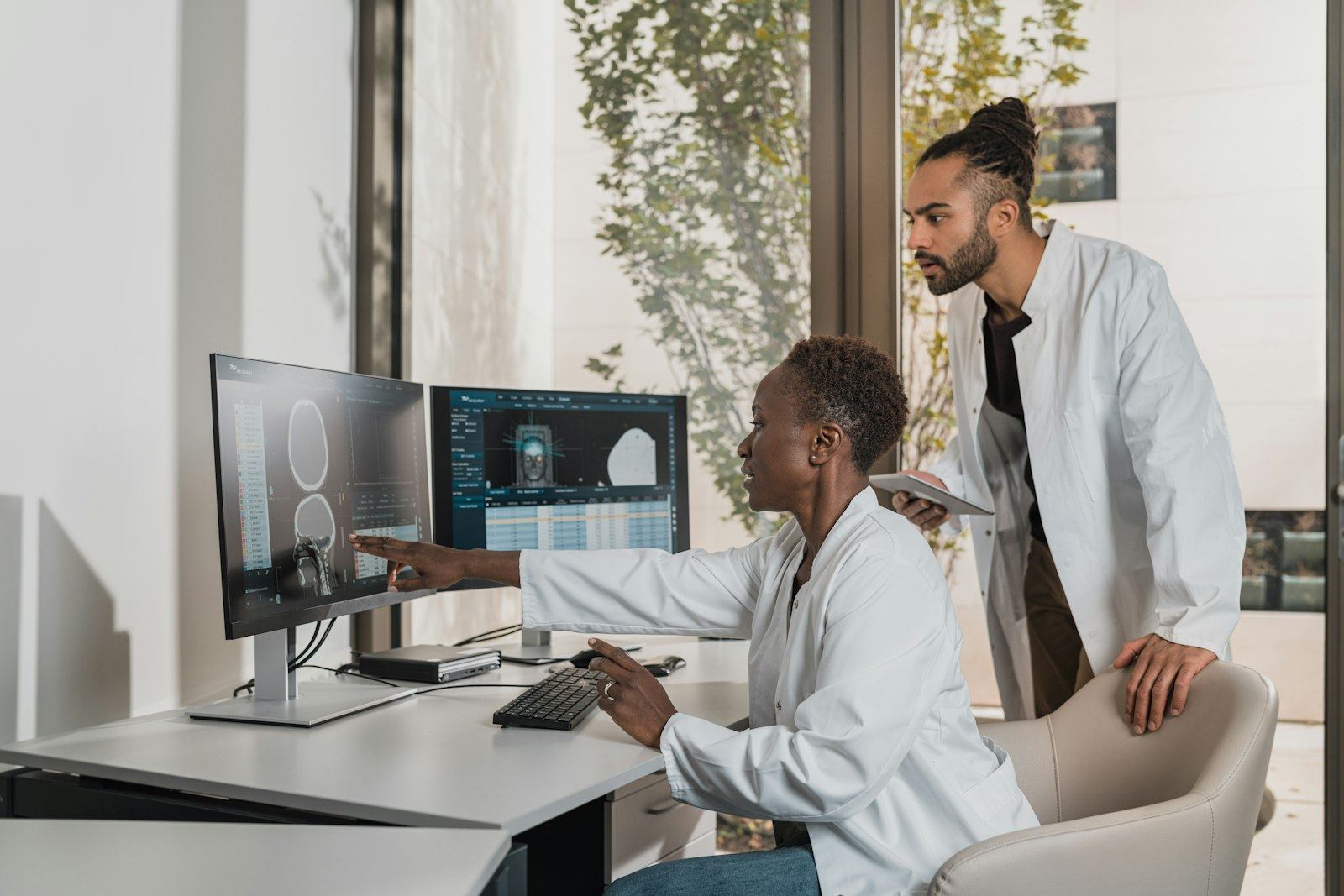 Two clinicians reviewing patient scans on desktop monitors
