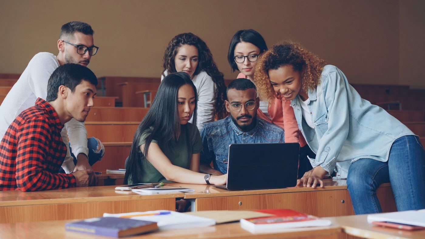 Group of students working together around a laptop in a lecture hall