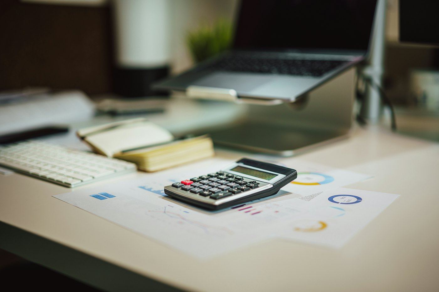 Calculator and financial reports on a desk beside a laptop