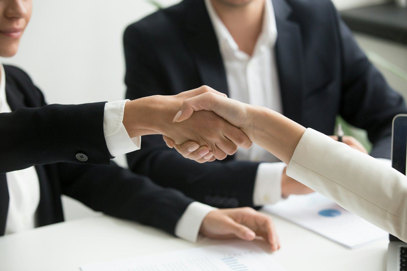 Two people shaking hands across a desk after closing a deal